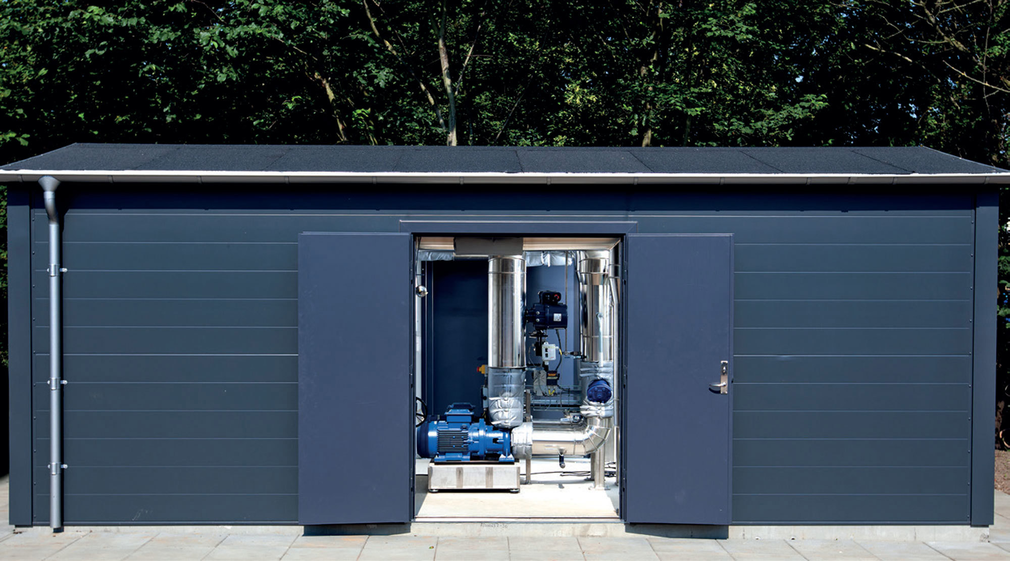 Liten blå byggnad med öppna dörrar som avslöjar industriella pumpar och rör inuti.