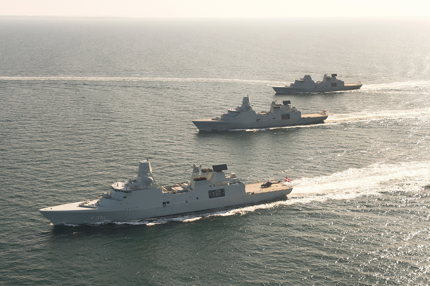 Three naval ships sailing in formation across a vast open sea.