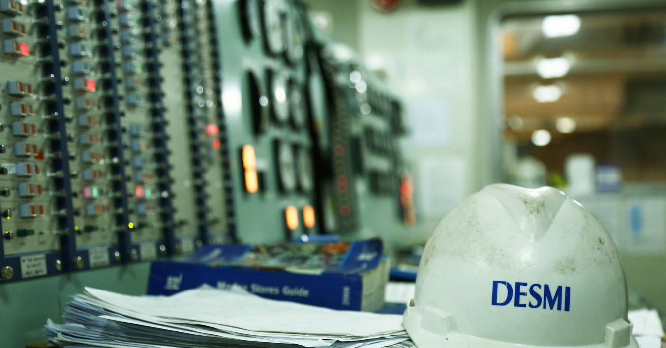 Casque de protection DESMI sur un bureau dans la salle de contrôle avec des panneaux d'équipement.