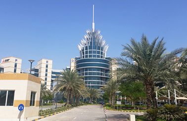 Modern building with unique spire design, surrounded by palm trees and clear sky.