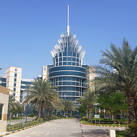 Modern building with unique spire design, surrounded by palm trees and clear sky.