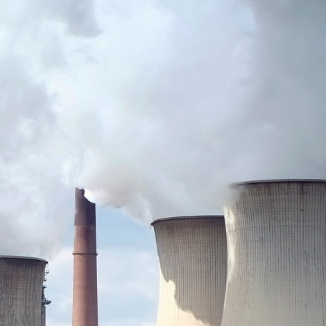 Cooling towers emitting steam at an industrial power plant against a cloudy sky.
