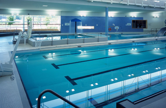 Indoor swimming pool with diving boards, basketball hoop, and bright overhead lighting.
