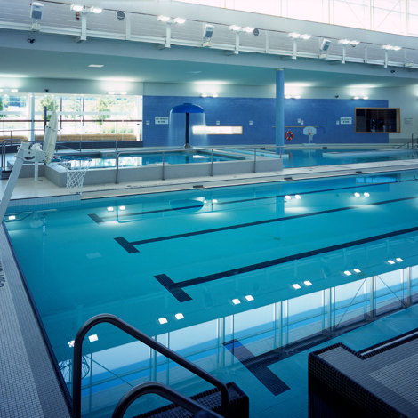 Piscina cubierta con trampolines, aro de baloncesto e iluminación brillante superior.