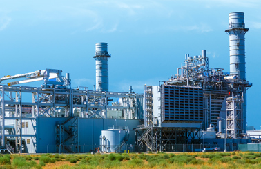Industrial power plant with large chimneys and metal structures under a clear sky.