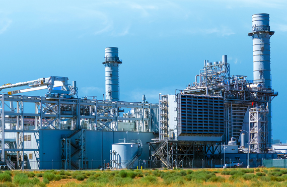 在晴朗的天空下，工业电厂设有大型烟囱和金属结构。