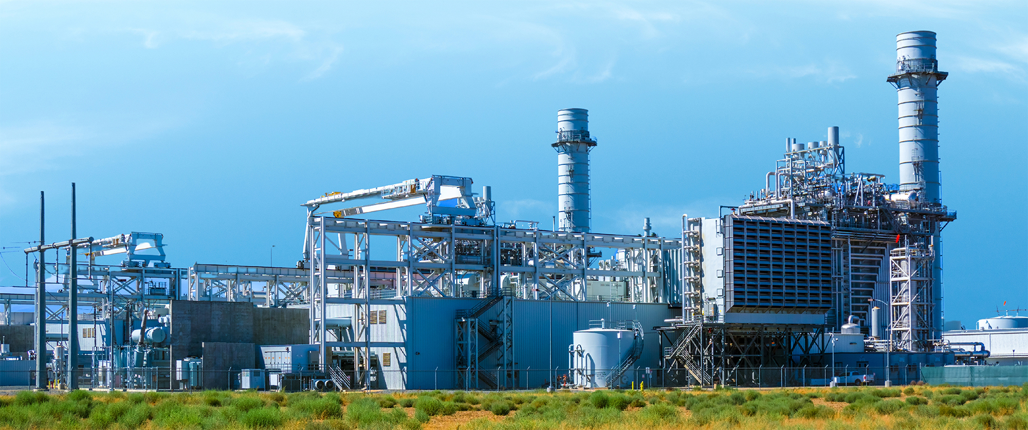 Industrial power plant with large chimneys and metal structures under a clear sky.