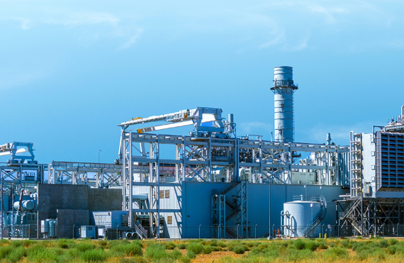 Industrial power plant with large chimneys and metal structures under a clear sky.