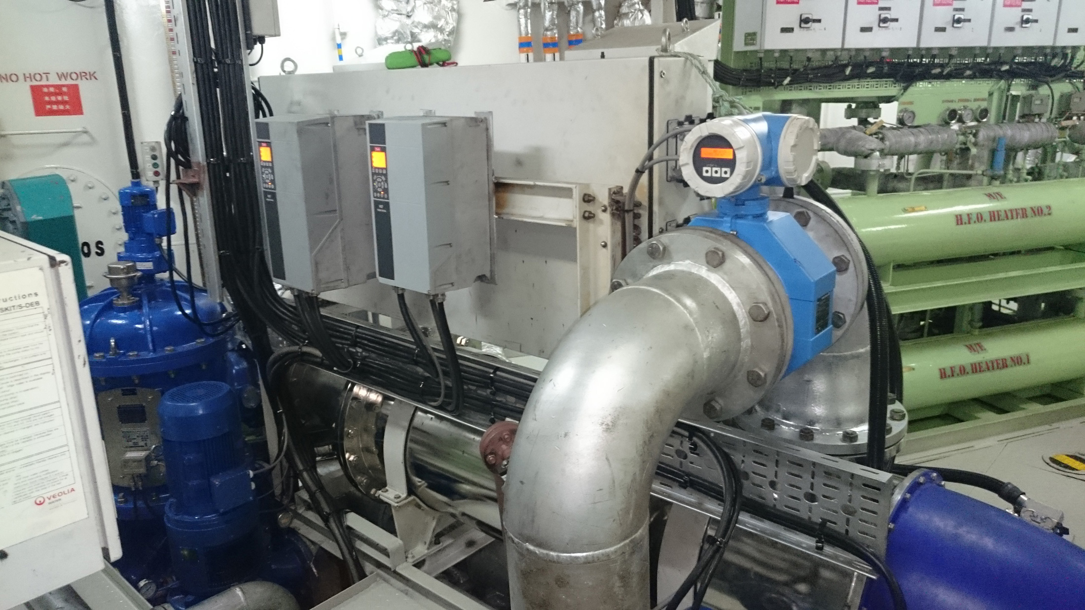 Industrial machinery setup featuring piping, control panels, and H.F.O. heaters in a facility.