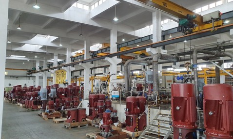 Industrial facility with multiple red pumps and overhead cranes for fluid handling.