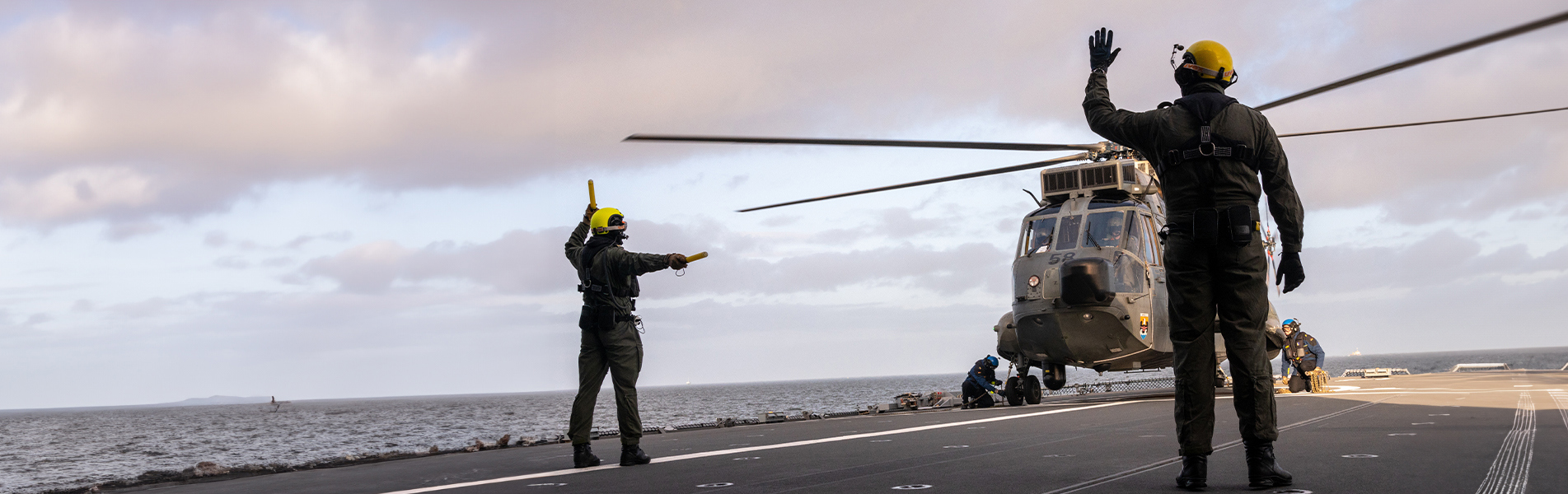 Besetningsmedlemmer på flydekket veileder helikopterlanding på et hangarskip til sjøs.