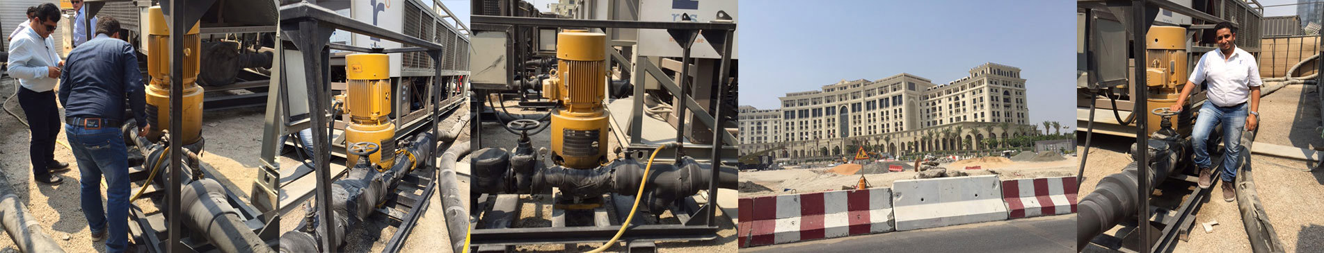 Men inspecting industrial pumps on a construction site near a large building.