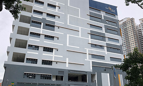 Modern multi-story building with geometric design and trees in foreground.