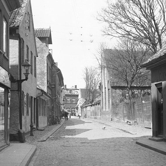 Historic cobblestone street with old buildings, bicycles, and a few people walking.