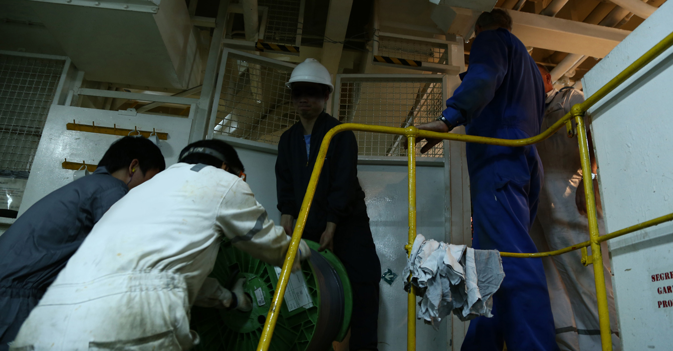 Workers move heavy equipment in an industrial setting with protective gear.