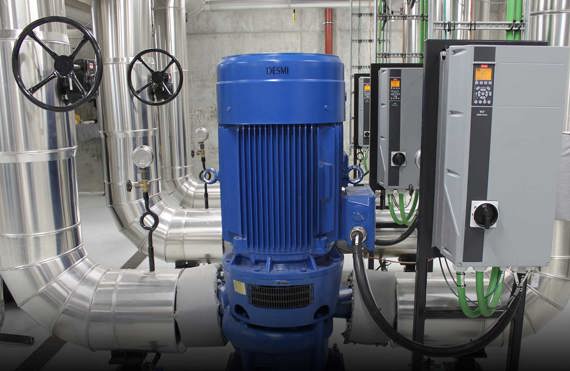Blå DESMI-pump med kontrollpaneler och rör i en industriell anläggning.
