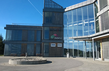 Modern glass building with DESMI and HomeNet logos, under clear blue sky.