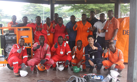 Group of workers in orange uniforms with DESMI equipment, giving thumbs up.