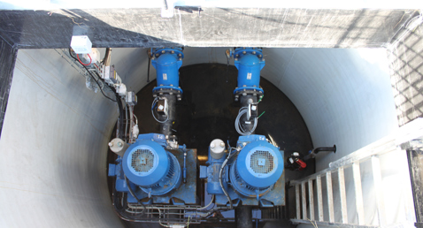 Blue industrial pumps in a cylindrical underground chamber with ladder access.