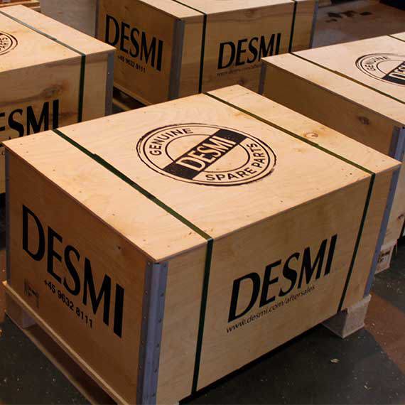 Trälådor märkta "DESMI Genuine Spare Parts" staplade på pallar.