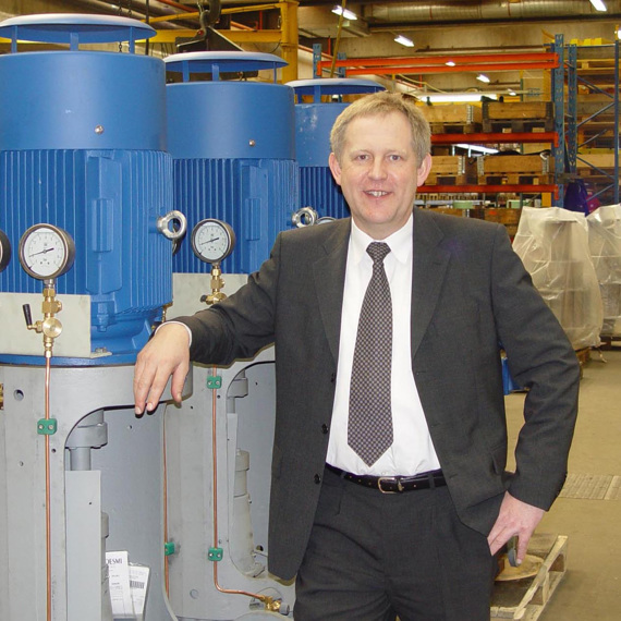 Man in suit standing beside DESMI pumps in an industrial setting.