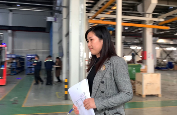 Woman holding documents walks through an industrial warehouse setting.