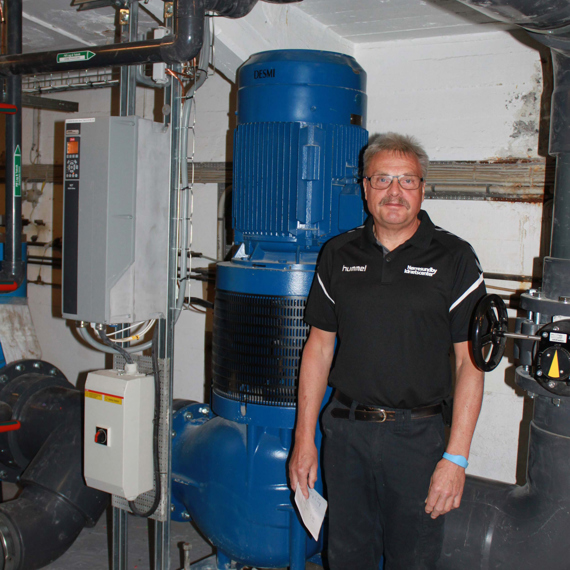 Man standing beside a large blue DESMI pump for fluid handling.