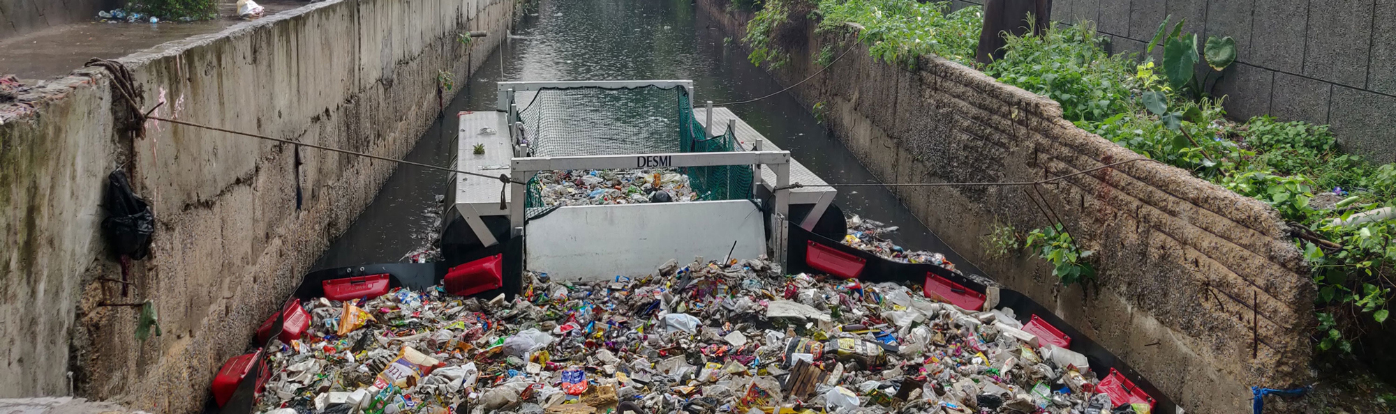 DESMI trash collector in a canal filled with floating garbage and debris.