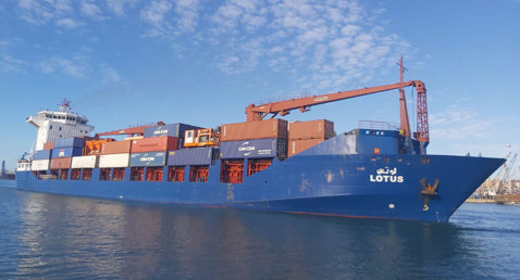 Blue cargo ship "Lotus" carrying stacked containers on a sunny day.