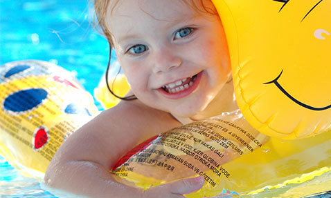 Lächelndes Kind mit aufblasbarem Spielzeug in einem Schwimmbecken.
