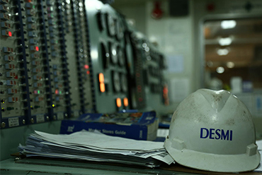 Casque de sécurité DESMI sur le bureau du panneau de contrôle dans un environnement industriel.