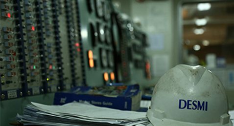 DESMI hard hat on control panel desk in industrial setting.