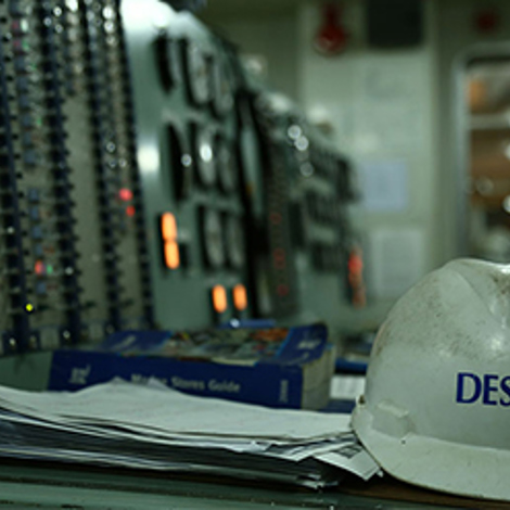 Casque de sécurité DESMI sur le bureau du panneau de contrôle dans un environnement industriel.