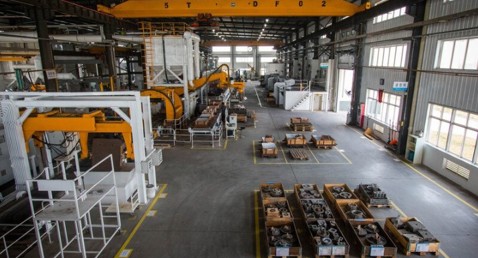 Industrial warehouse with machinery, overhead crane, and organized pallets of equipment.