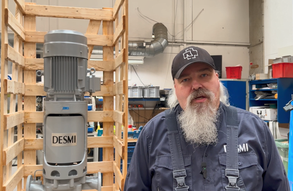 Man standing beside a DESMI pump in an industrial workshop setting.