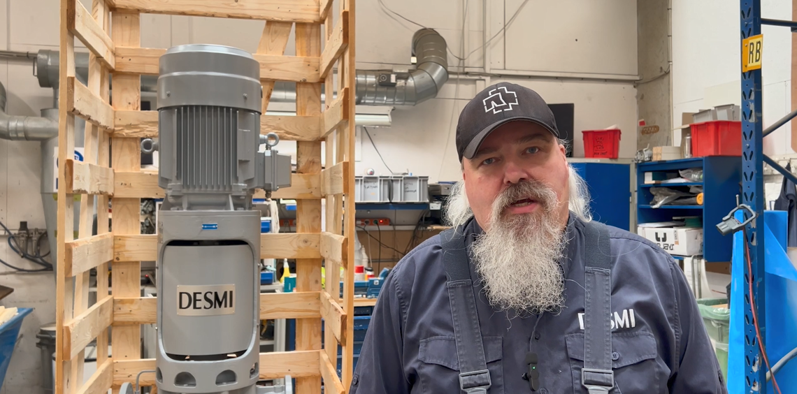 Man standing beside a DESMI pump in an industrial workshop setting.
