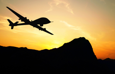 Silhouette of a drone flying over mountains during sunset.