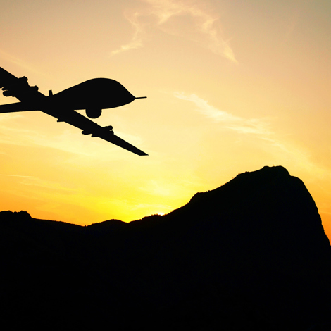 Silhouette of a drone flying over mountains during sunset.