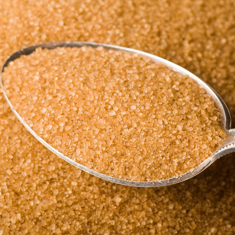Łyżka granulowanego brązowego cukru na stosie luźnych kryształów cukru.