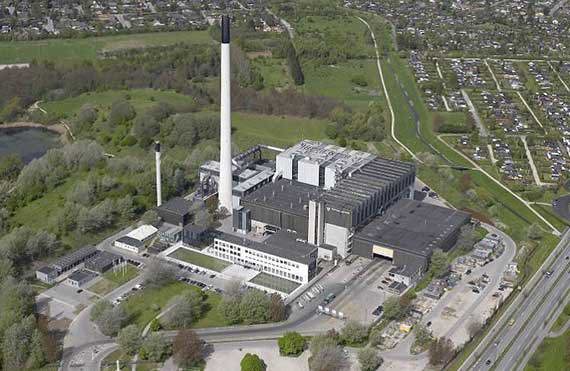 Widok z lotu ptaka na duży obiekt przemysłowy z wysokimi kominami, otoczony zielenią.