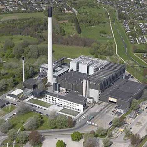 Aerial view of a large industrial facility with tall chimneys and surrounding greenery.