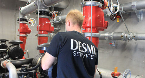 Technicien en chemise DESMI effectuant l'entretien des pompes et tuyaux industriels dans une installation.