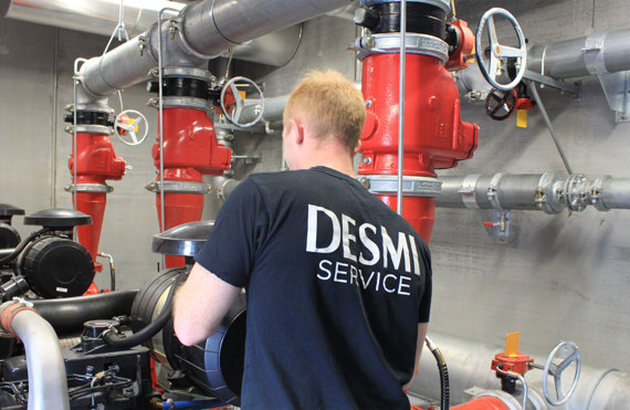 Technician in DESMI shirt servicing industrial pumps and pipes in a facility.