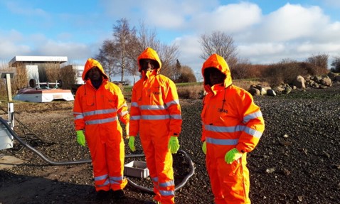 Three workers in orange DESMI gear and gloves in an outdoor setting.