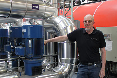 Man standing beside industrial pumps and piping in a mechanical setting.