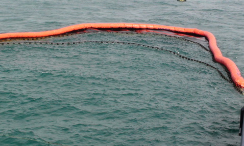 Oil containment boom in the ocean with a small boat nearby.