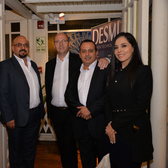 Four people in formal attire standing beside a DESMI banner indoors.
