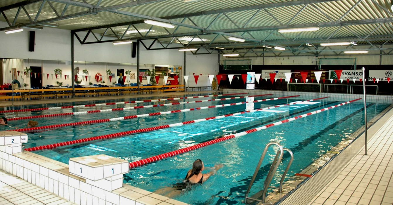 Indoor swimming pool with lanes, swimmer, and tiled deck area.