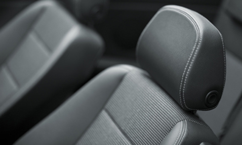 Primo piano di un sedile auto con rivestimento in pelle nera e cuciture visibili.