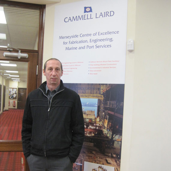 Man standing beside a Cammell Laird sign promoting engineering and marine services.
